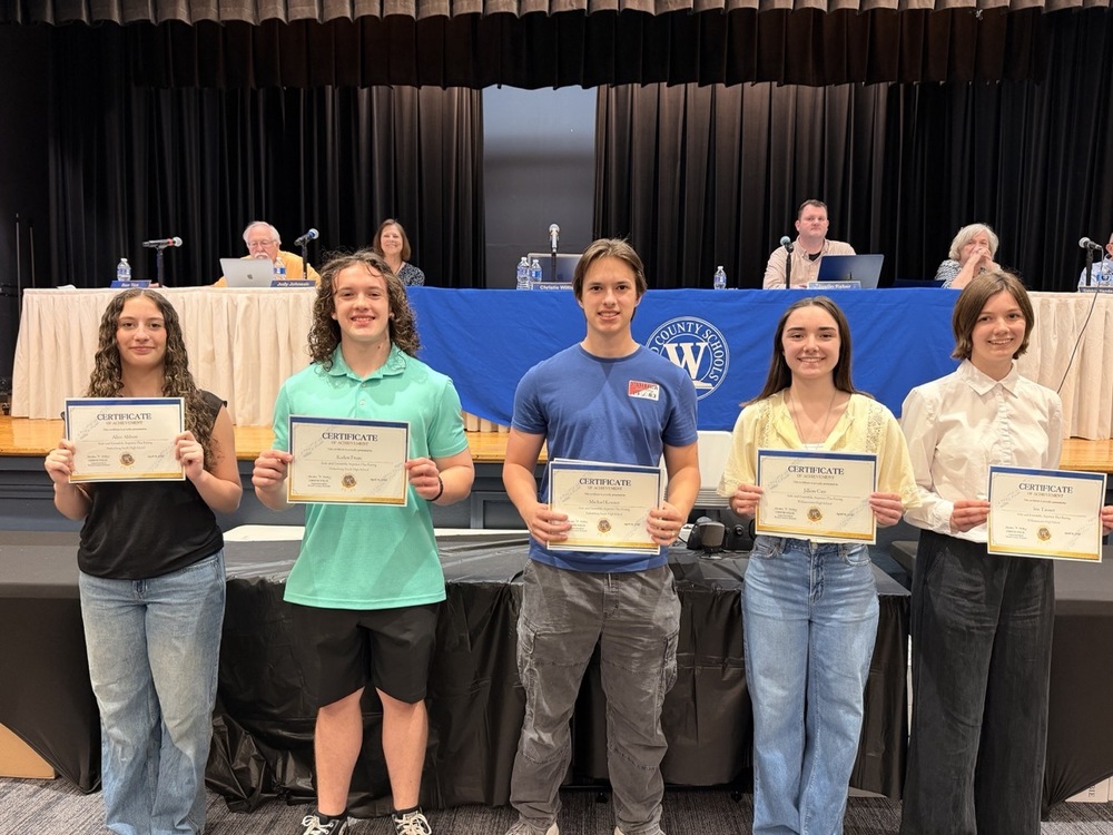 Five students holding certificates in front of Board of Education