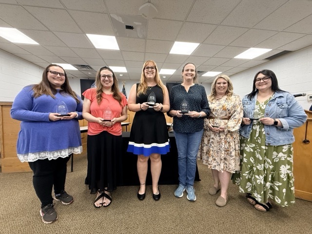Image is of six teachers standing and posing for picture holding a glass recognition for being National Board Certified Teachers