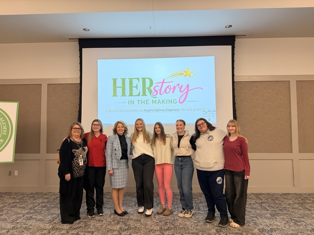 Senior woman standing with superintendent of Wood County Schools in front of a projector screen with the words HERstory: in the making
