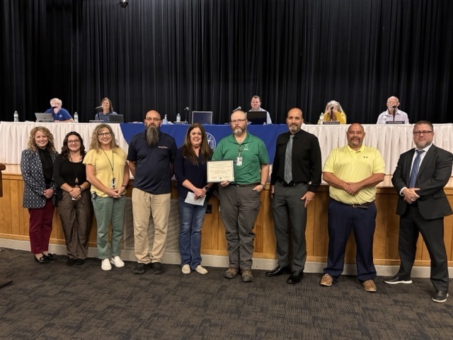 Staff standing in line receiving Board of Education Meeting recognition for ranking in top 15 of state