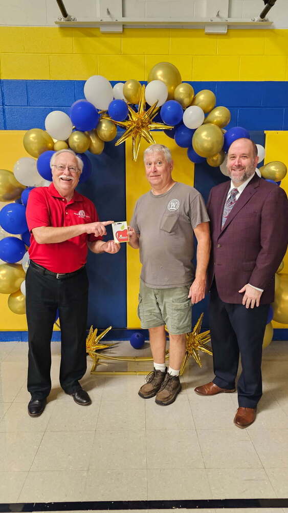 image of three men standing in a gymnasium with the center person holding a recently won gift card to Applebee's restuarant