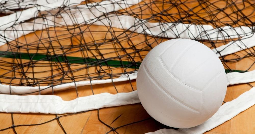 image of a volleyball laying on top of a volleyball net on the court floor