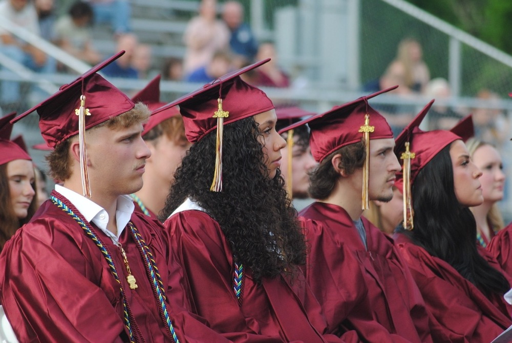 students at a high school graduation in caps and gowns looking on