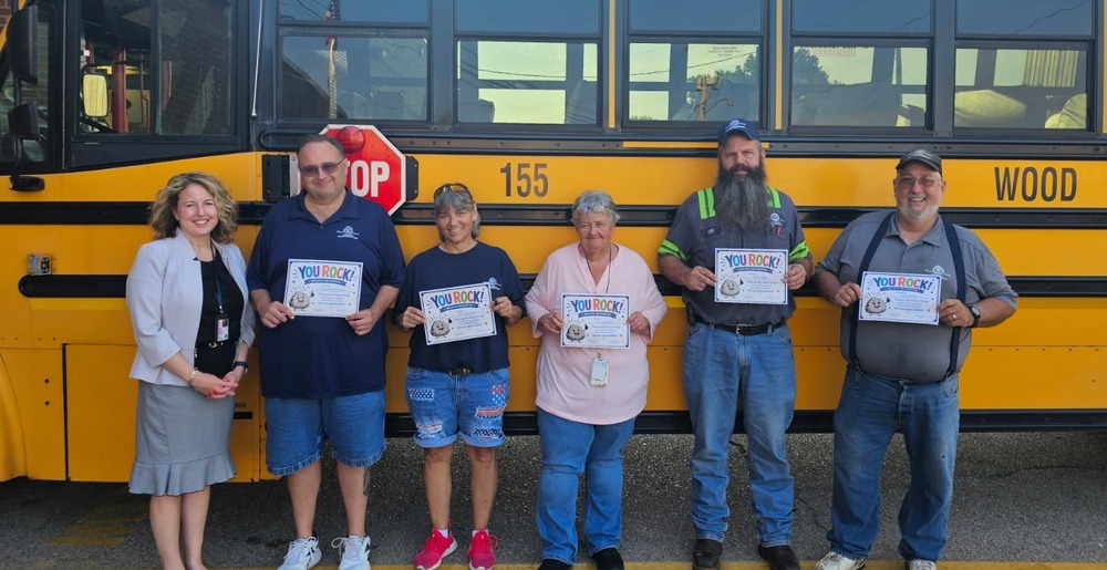 school superintendent and 5 members of the school bus transportation team holding certificates and standing in front of a yellow school bus