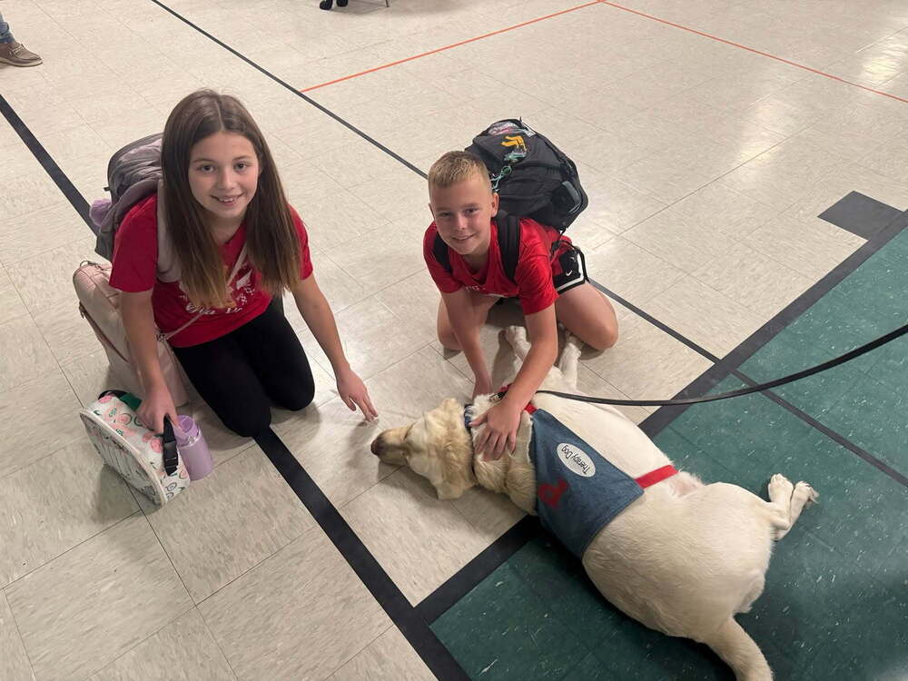 two students stooping on the floor petting a therapy dog