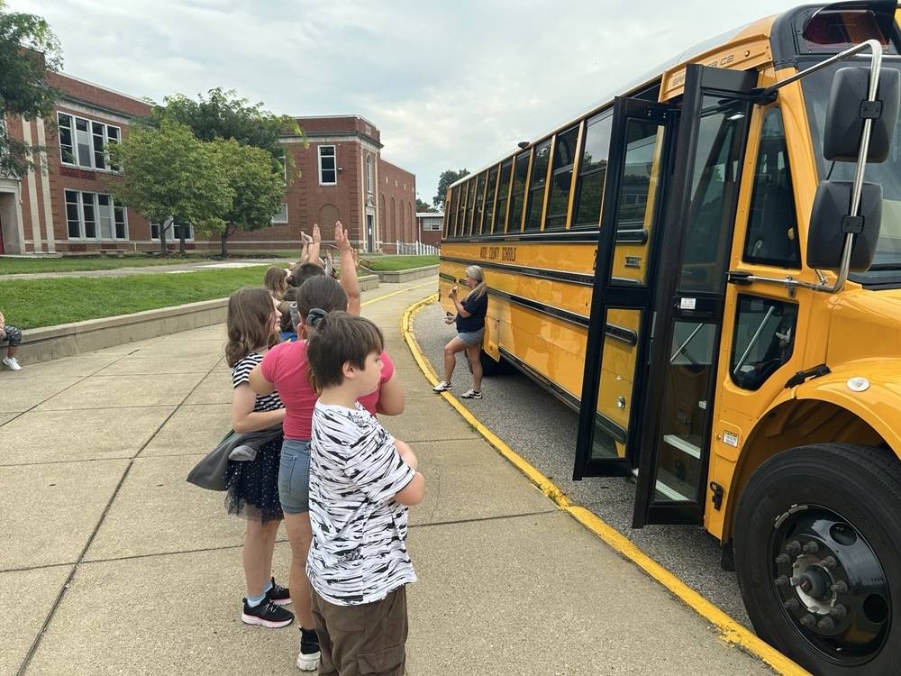 students standing in front of a school bus with a brick school building in the background
