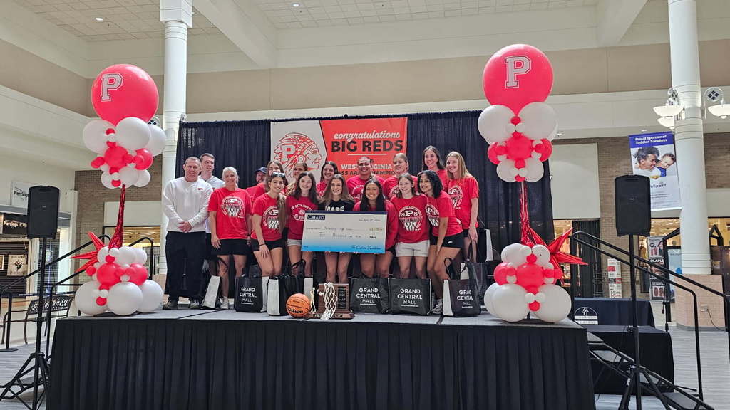 students and coaches standing on a stage in a  mall accepting a charitable check from owners of mall