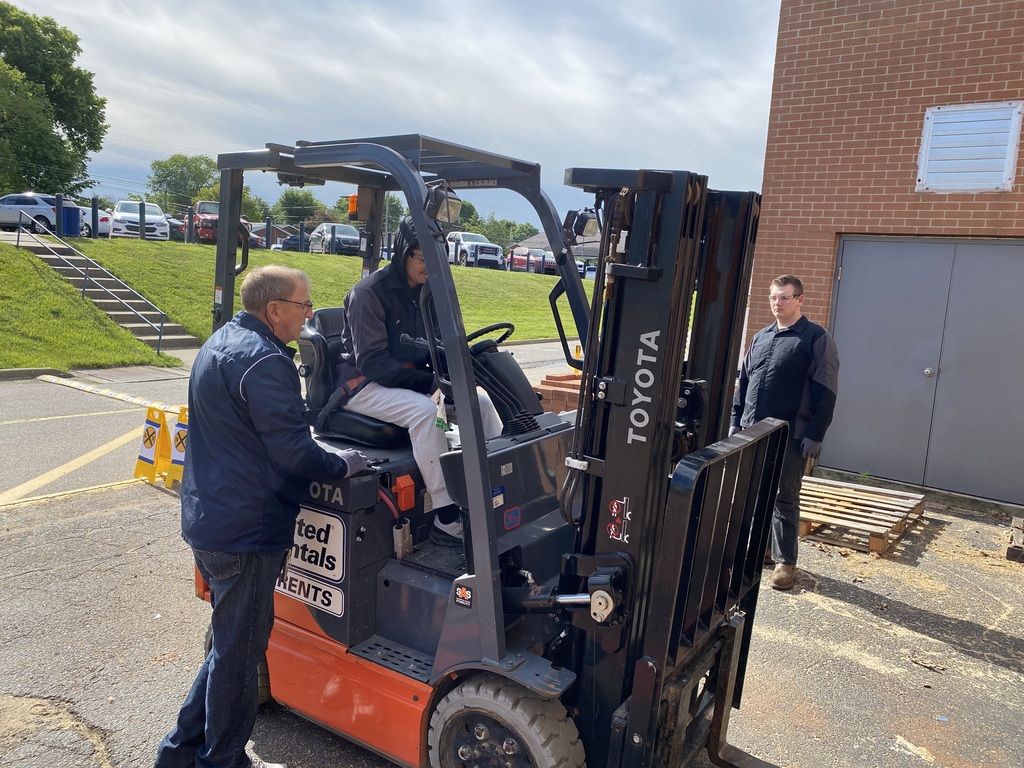 Image of student operating a forklift while teacher assists.