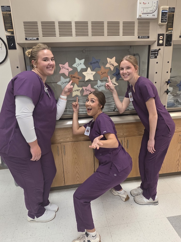 Students are wearing matching purple medical scrubs pointing at stars.