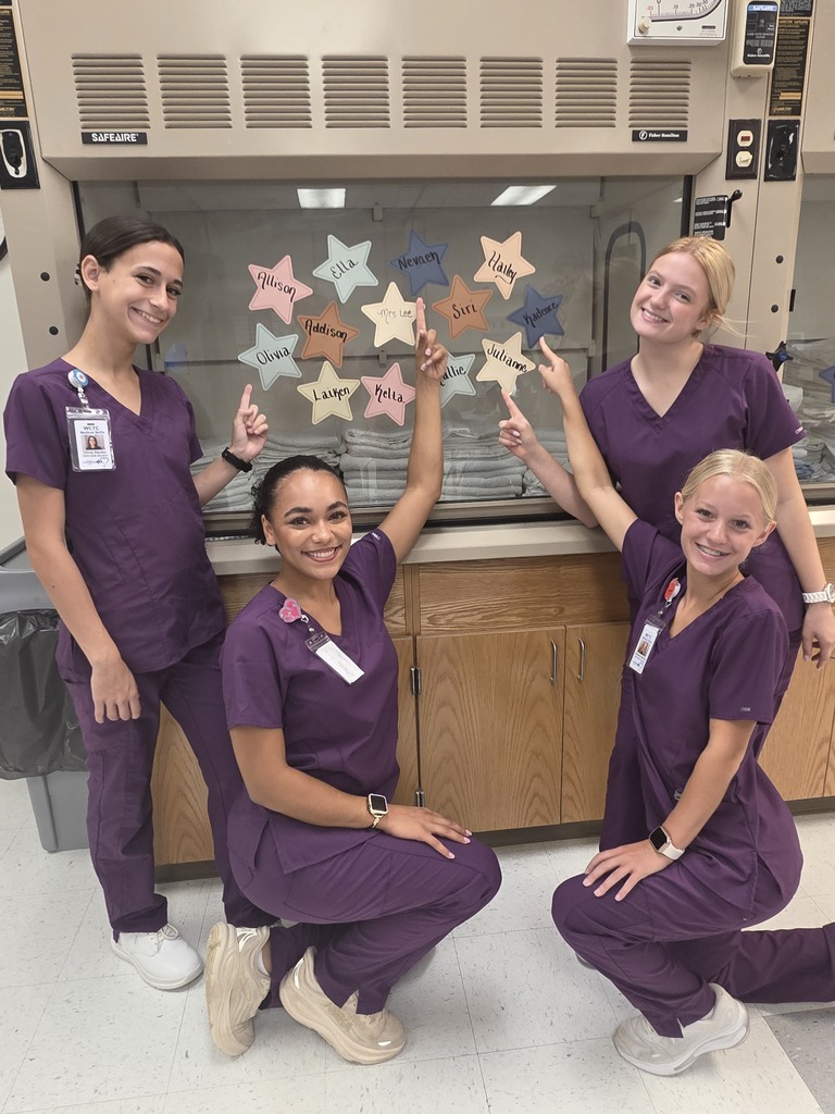 Students are wearing matching purple medical scrubs pointing at stars.