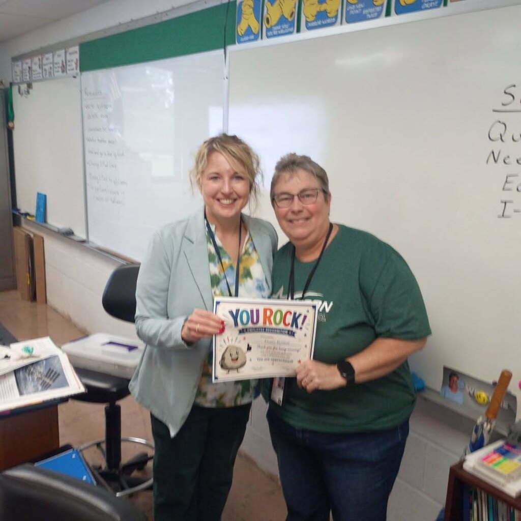two women standing and holding a certificate in a classroom