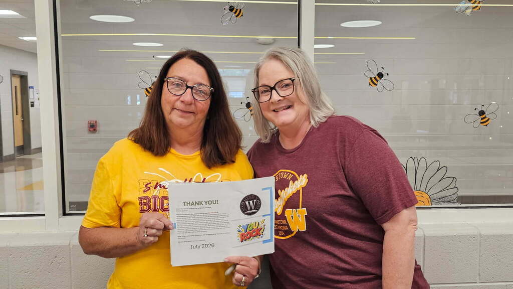 two women in a school office holding a certificate for the camera