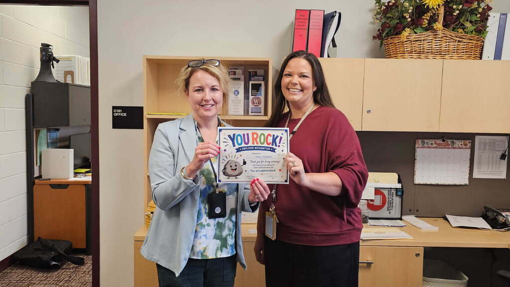 two women holding a certificate in a school office
