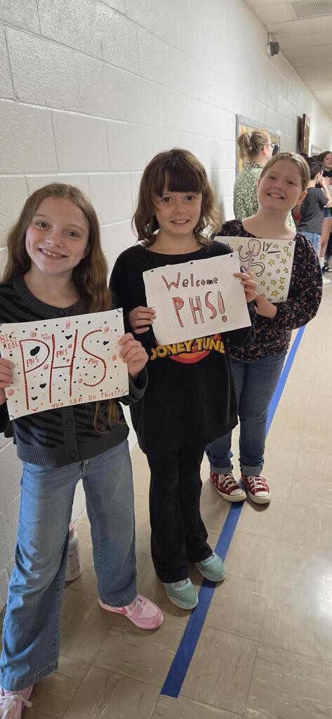 Three girls holding signs and cheering for the high school.