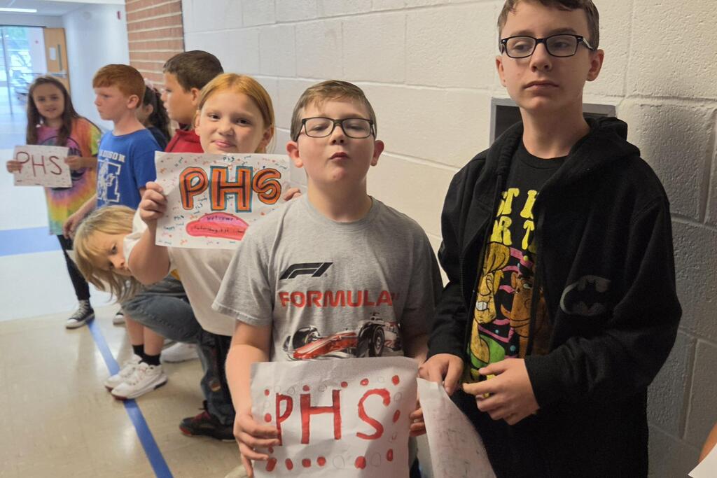 Students smiling and holding signs as they wait for the high school band.