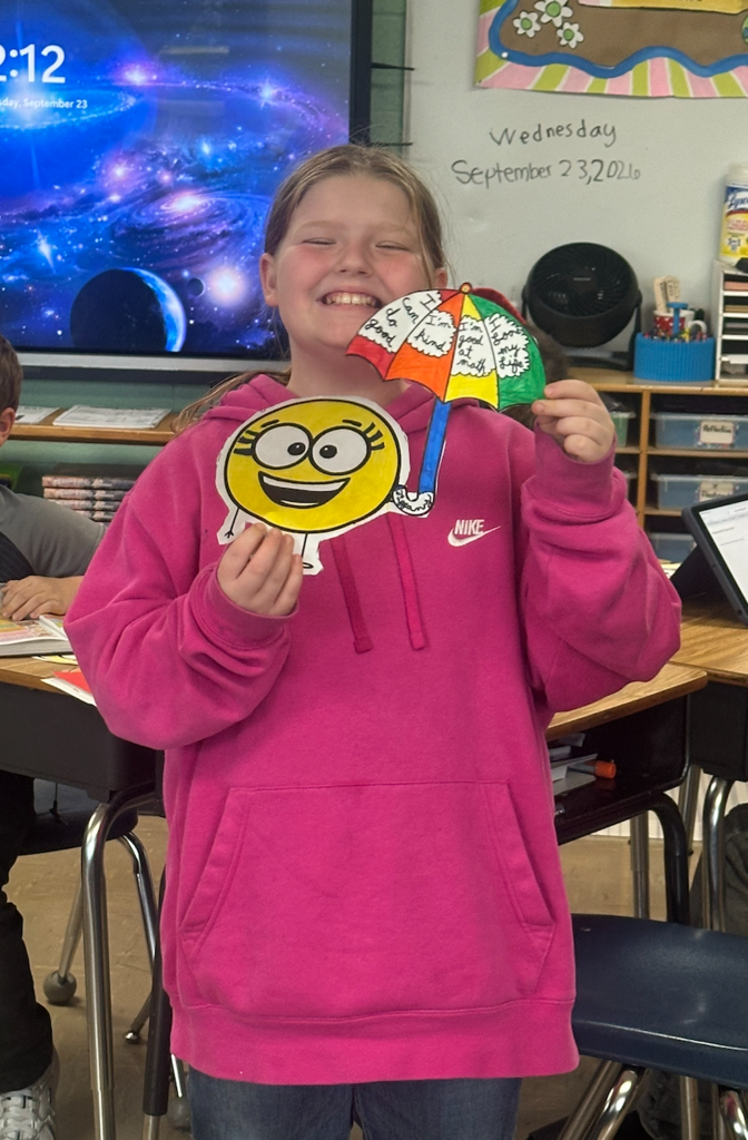 Girl holding her little spot of optimism artwork and smiling.