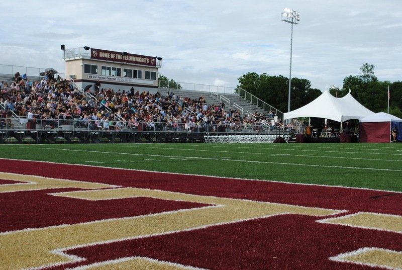 football field with people in stands in the distance waiting for a graduation ceremony