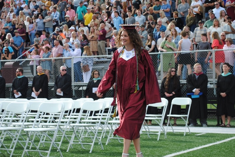 student, smiling, walking toward her seat for a high school graduation ceremony