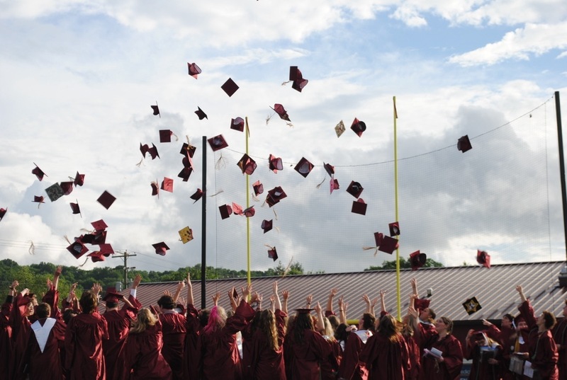 in a large group, students at high school graduation throwing caps into the air
