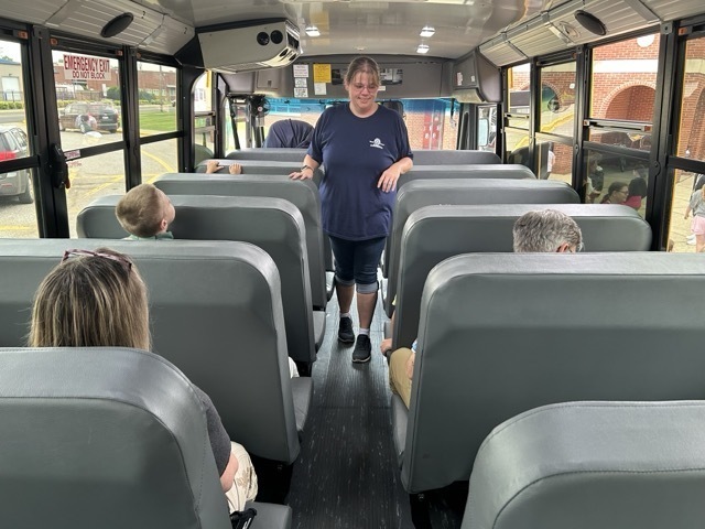 woman standing facing seated children on a school bus