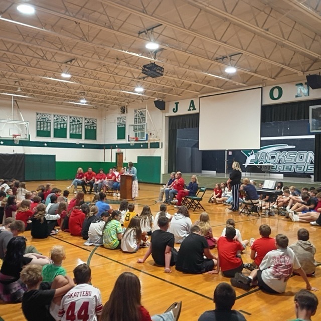 middle school students seated in gymnasium listening to a speaker at a podium