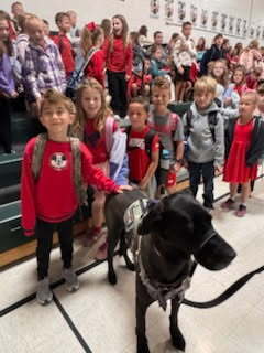 students posing with a dog with additional students on bleachers in the background