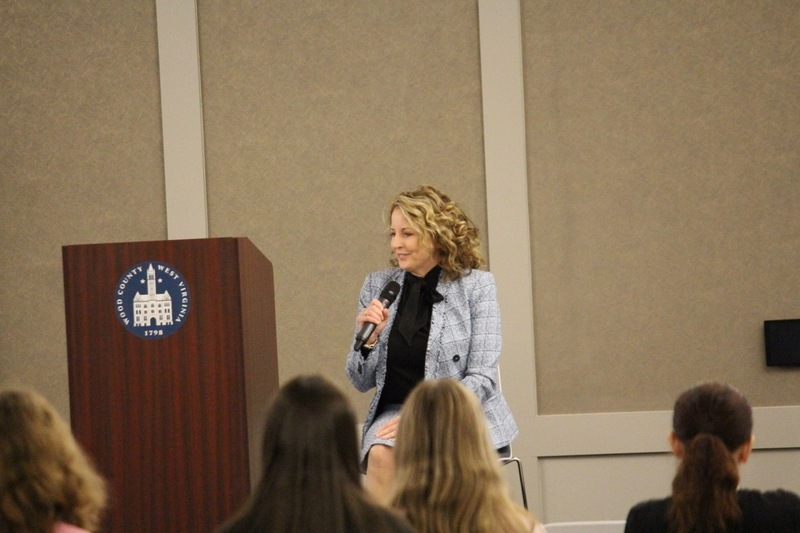 Superintendent of Wood County Schools speaks to area, senior women sitting on a small stage, holding a microphone