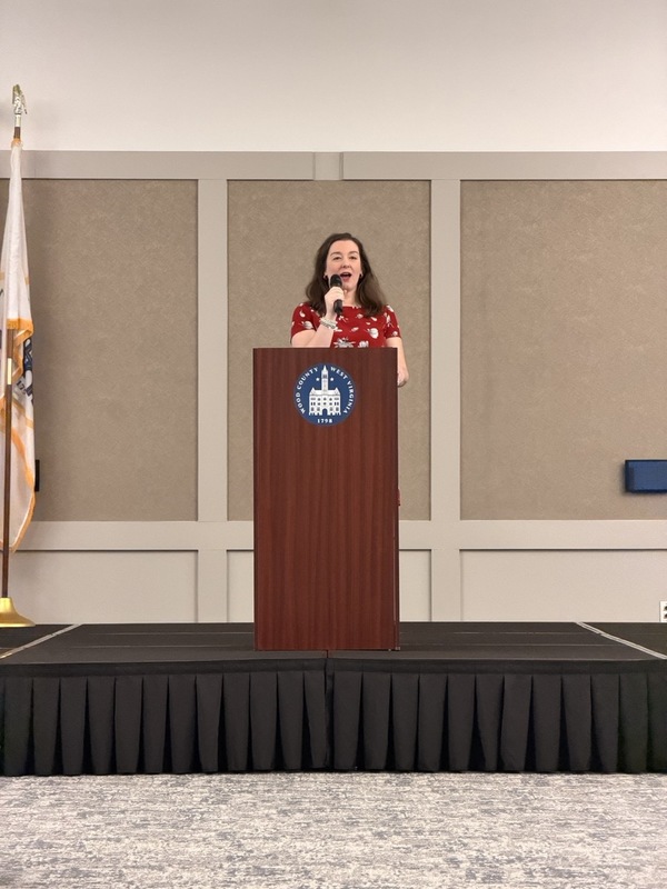 Woman standing on platform in red dress, holding a microphone