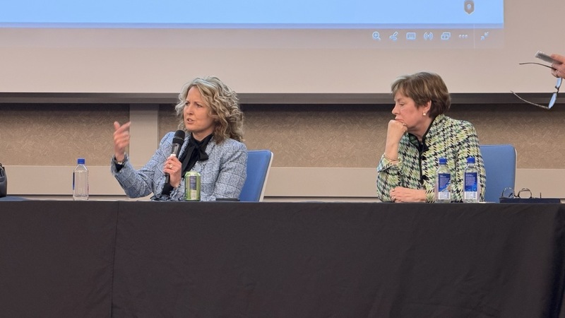 Two women, as part of the panel, taking questions from the audience while seated at a table