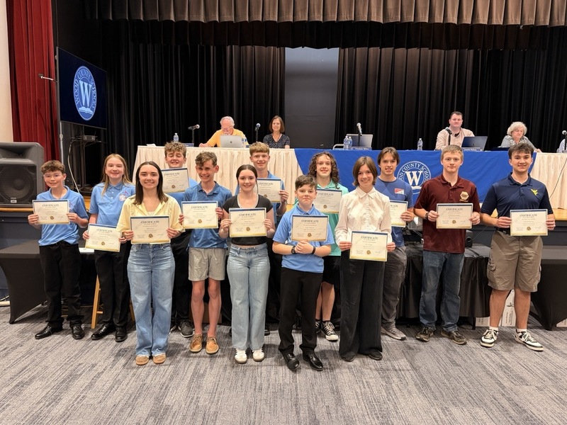 Group of students receiving an award and holding their certificate in front of the Board of Education