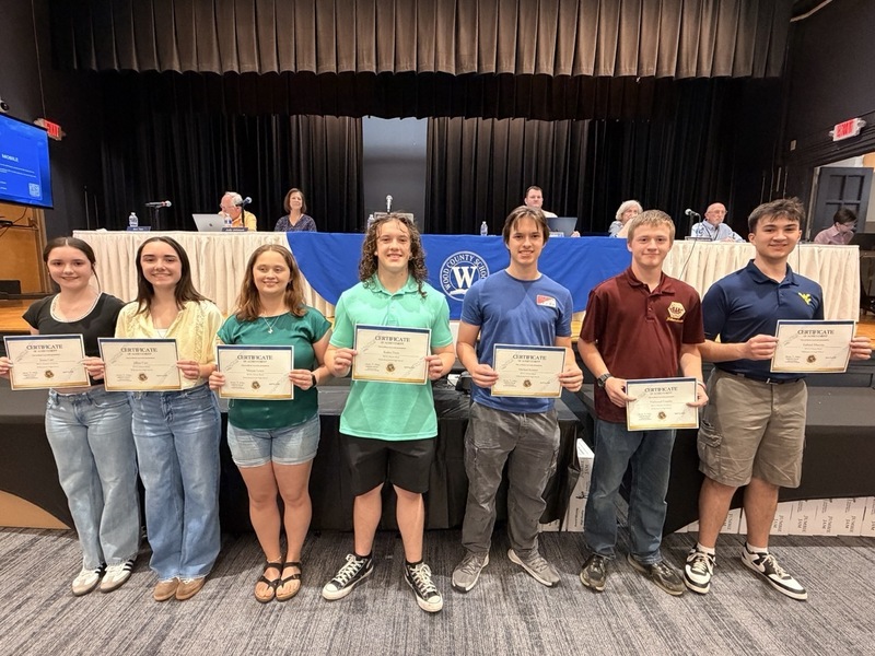 Group of students receiving awards and holding their certificates in front of the Board of Education