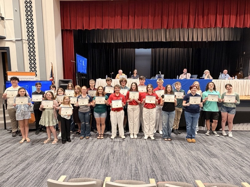 Group of students receiving an award and holding their certificate in front of the Board of Education