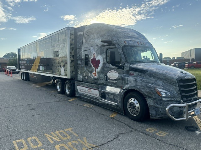 image of a semi truck parked in a high school parking lot with blue skies and light clouds above. The school campus off in the distance.