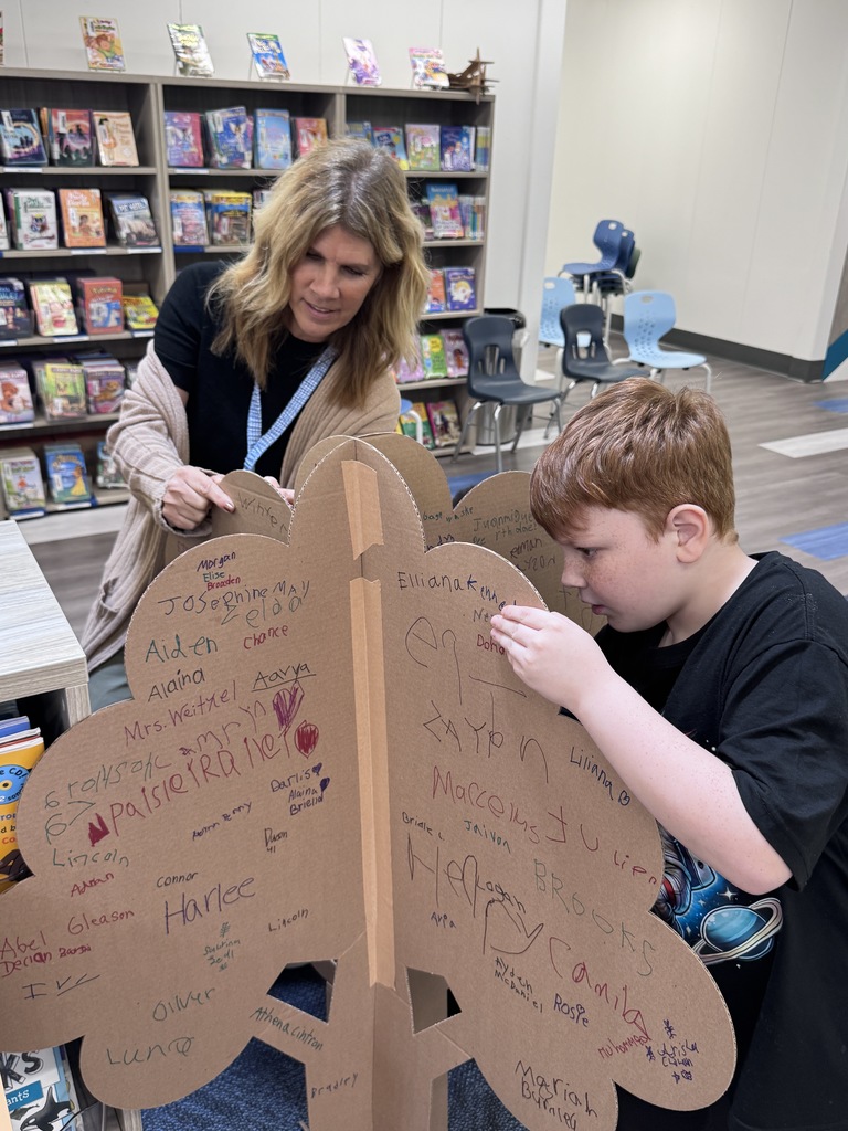 student and teacher signing a cardboard tree