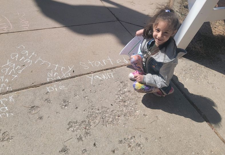 Student knelt down on the sidewalk next to her chalk drawn words