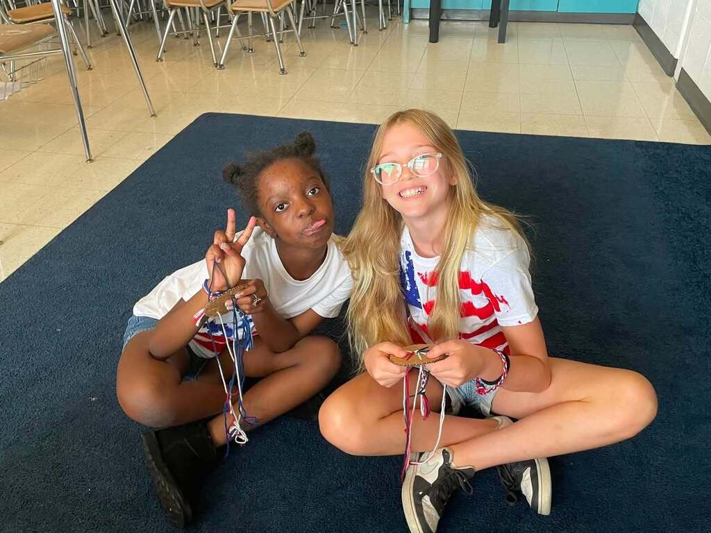 two smiling students making friendship bracelets 