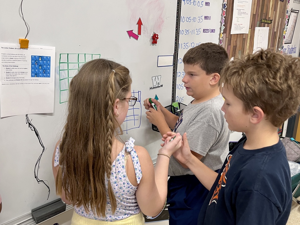 Students work together to solve a complex math problem on the whiteboards around the classroom
