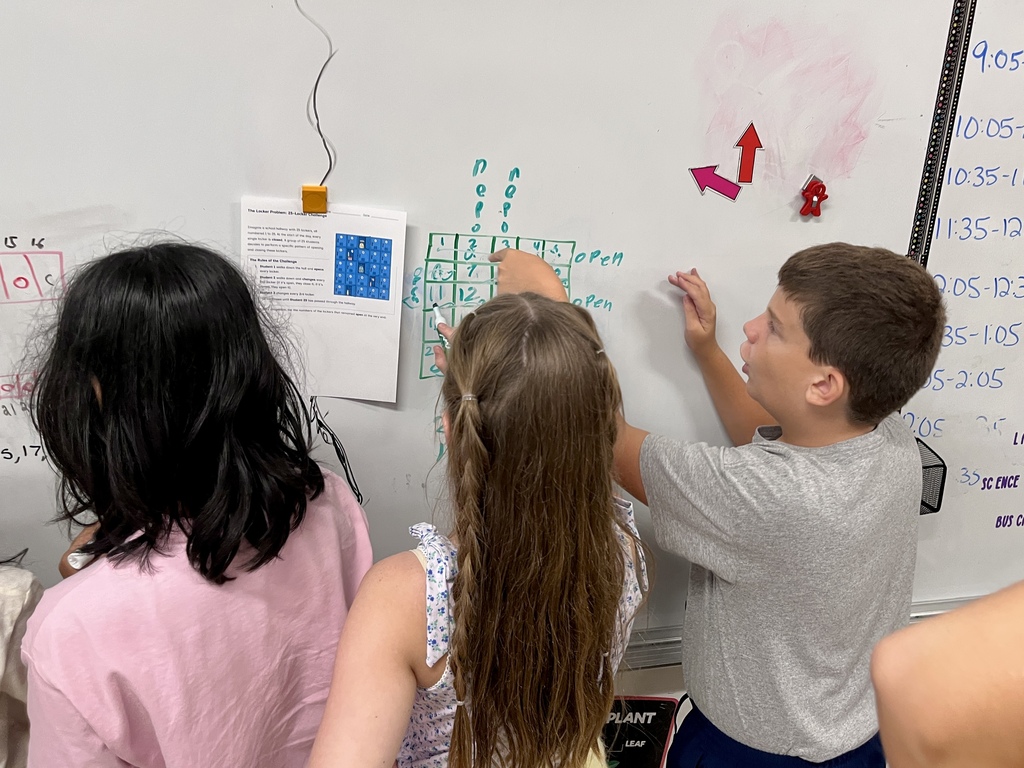 Students work together to solve a complex math problem on the whiteboards around the classroom