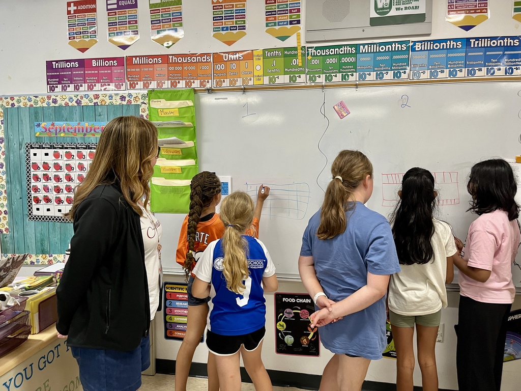 Students work together to solve a complex math problem on the whiteboards around the classroom
