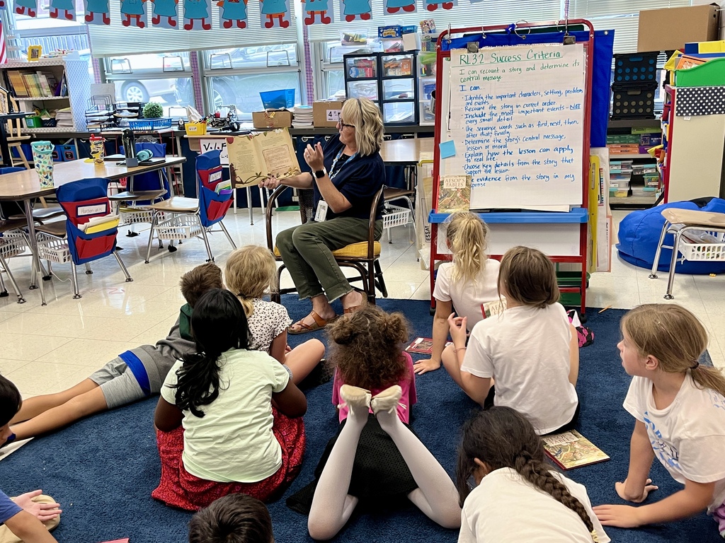 Teacher reads to students gathered on the rug in classroom