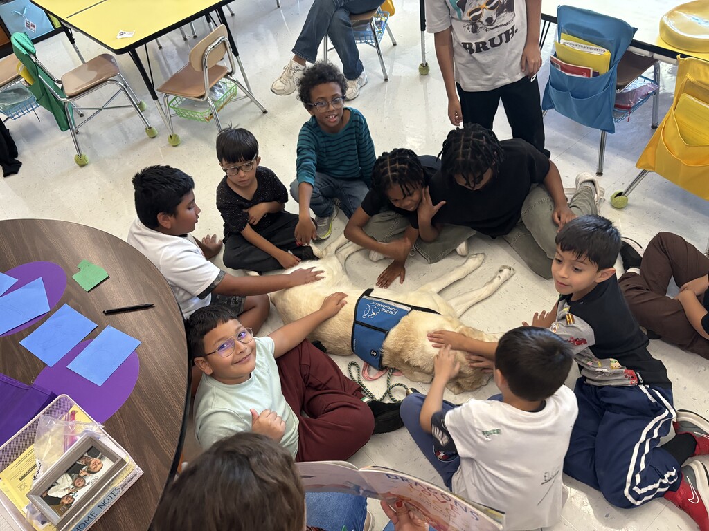 students sit in a circle around a service dog while teacher reads a story