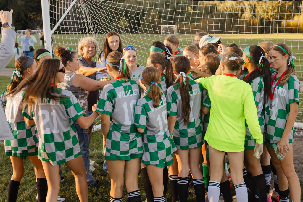 girls soccer team put their hands in to celebrate