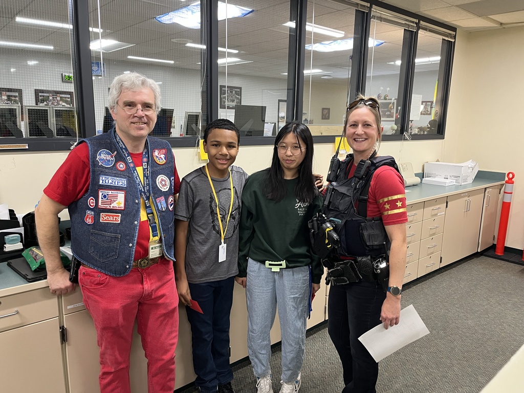 A teacher, two students, and a police officer pose for a photo in the office