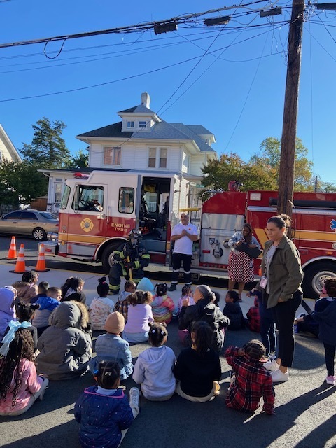 fire chief and truck in front of students sitting on the ground learning about fire prevention