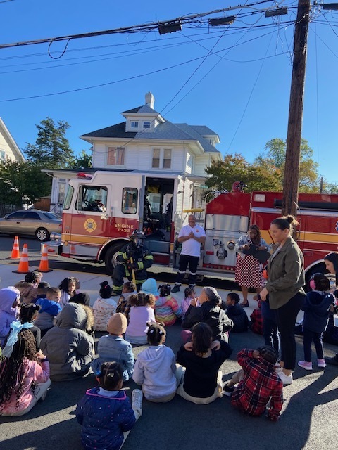 fire chief and truck in front of students sitting on the ground learning about fire prevention