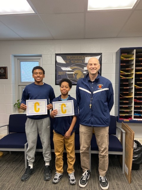 two students holding athletic awards with coach
