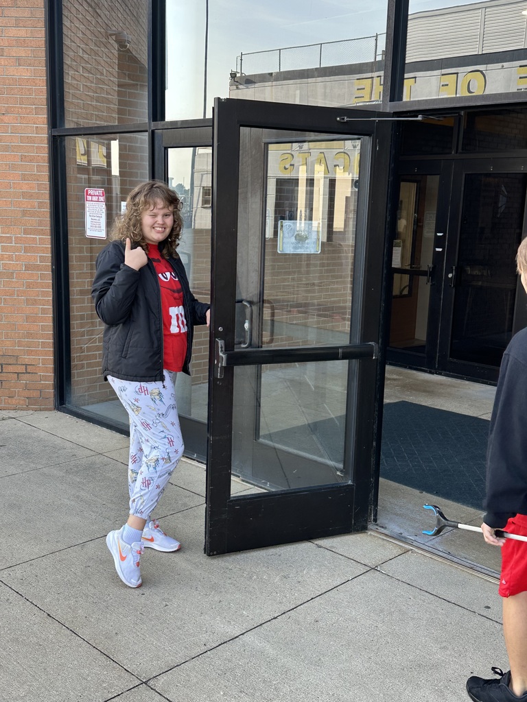 A student holding open the door for the other classmates to reenter the building.