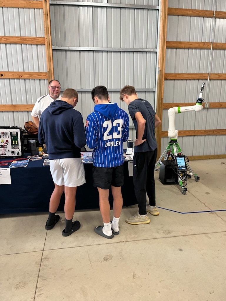 Students interacting with a presenter at the Career Showcase. They are looking at a table with materials and speaking with a presenter who is behind the table.