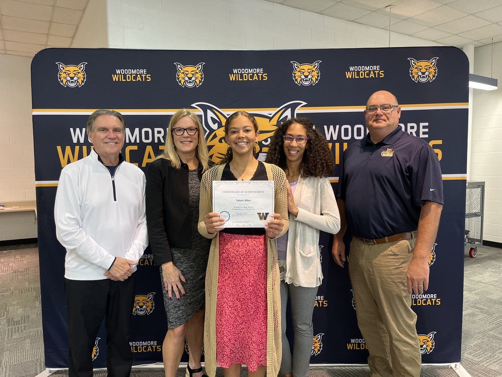 From left to right: Superintendent Mr. Mock, High School Principal Mrs. Coil, Satori and family, Board President Mr. Miller. They're all standing in front of the Woodmore Wildcats backdrop in the high school media center.