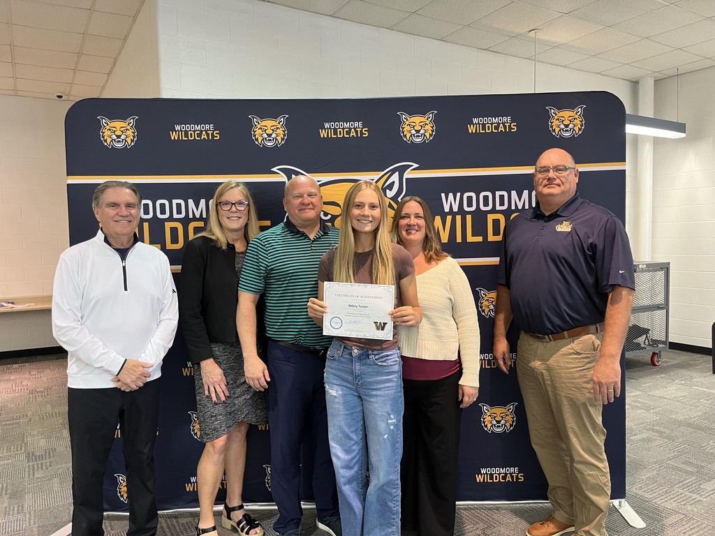 From left to right: Superintendent Mr. Mock, High School Principal Mrs. Coil, Abbey and family, Board President Mr. Miller. They're all standing in front of the Woodmore Wildcats backdrop in the high school media center.